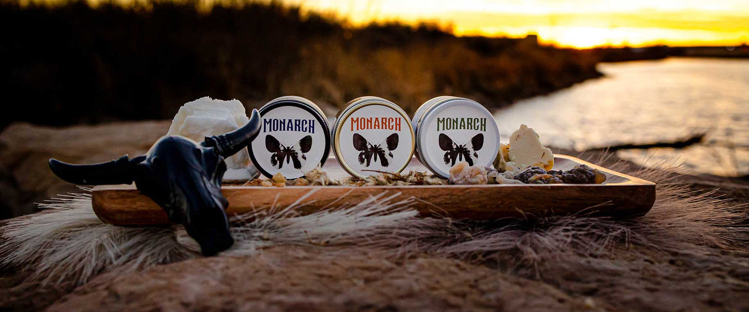 Monarch skincare products displayed on a wood plank with a sunset over a river as the background.
