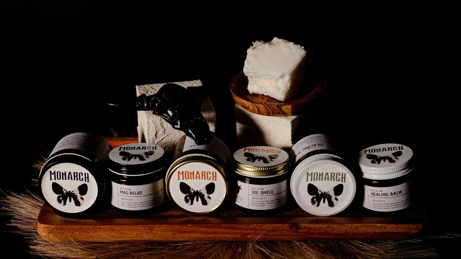 Collection of Monarch grass-fed beef tallow skincare products on a nice table display with some raw beef tallow in the background.